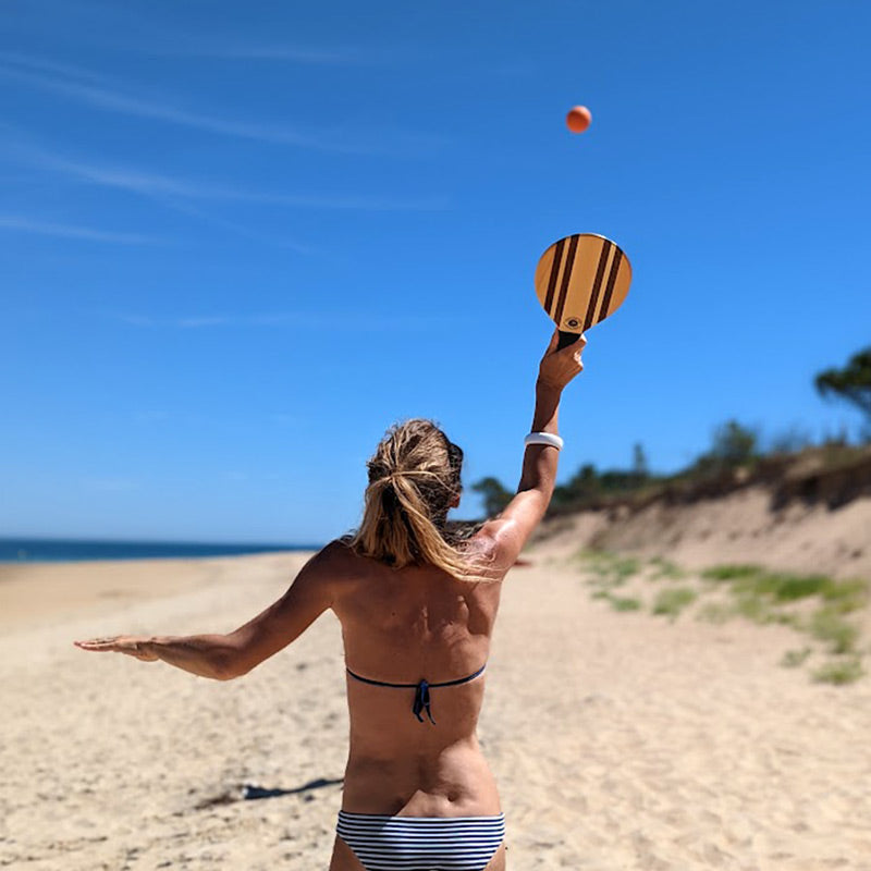 femme sur la plage entrain de jouer avec de belles raquettes en bois