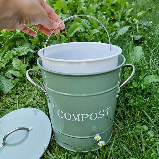 jolie poubelle à compost en métal coloris vert sauge posée sur l'herbe