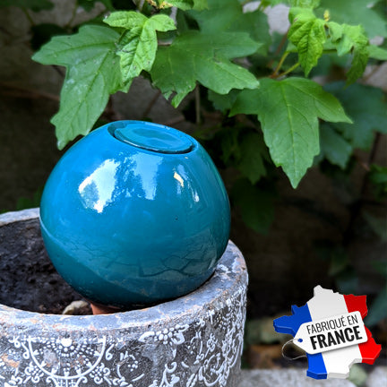 Jolie boule d'arrosage à planter dans un pot de fleur. la couleur bleu canard contraste avec les couleurs du pot et des plantes, formant un bel ensemble décoratif